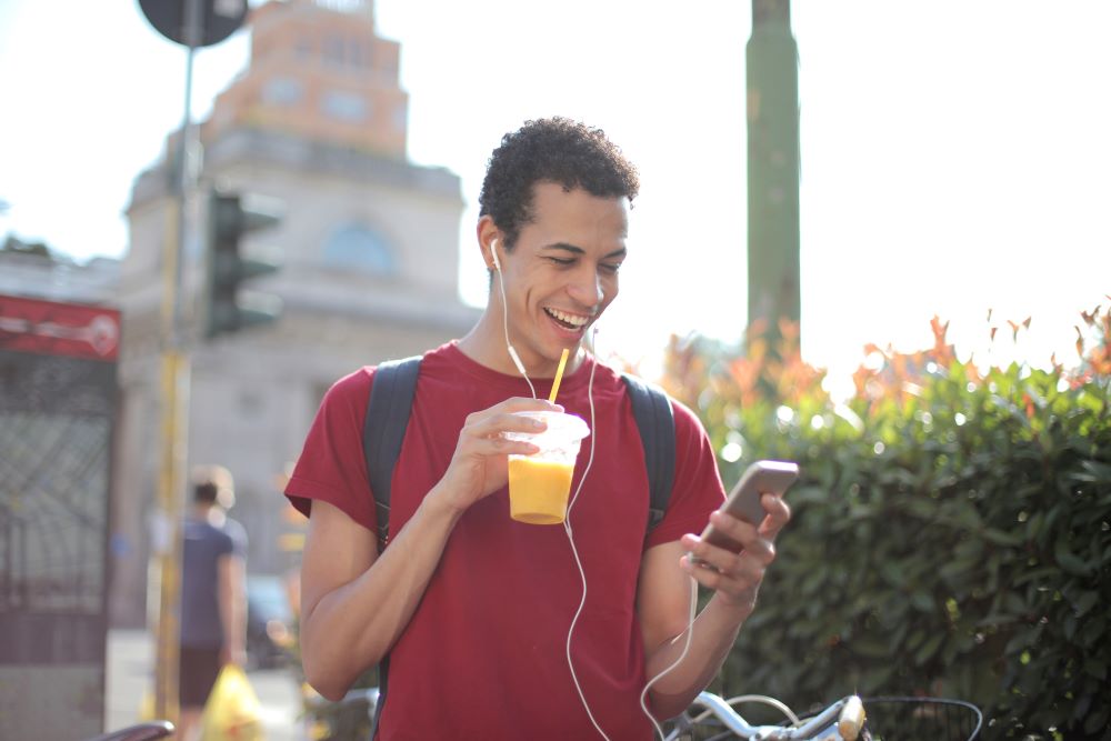 internet mobilny dla studenta - mężczyzna pijący sok korzystający z telefonu komórkowego